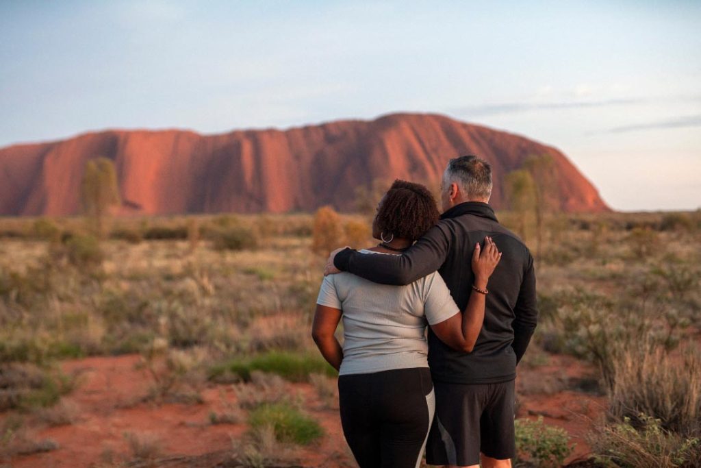 Couple enjoying the view of Uluru at sunrise. Australia's Northern Territory is wide open for adventures like this!