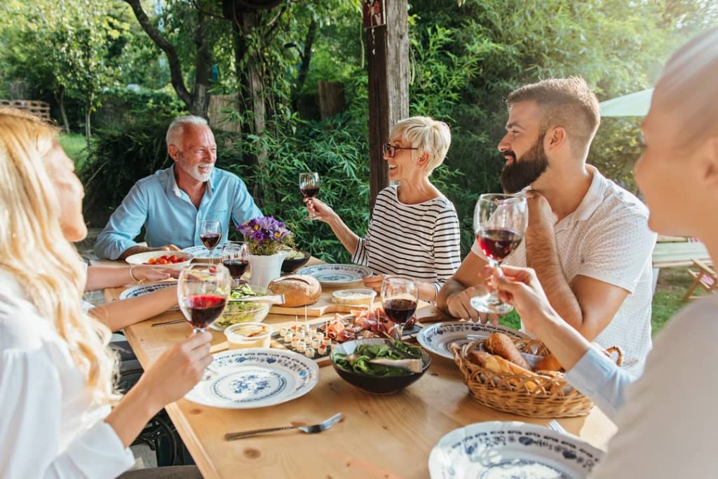 Family celebrating with red wine and delicious food at an outdoor dining table in Italy.